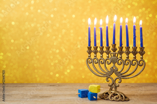 Jewish holiday Hanukkah background with vintage menorah and spinning top dreidel over lights bokeh.