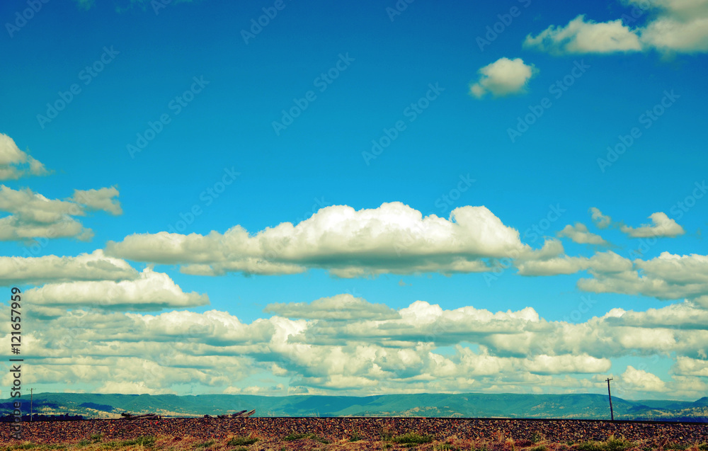 Rural cloudscape with flat road and power lines in foreground and mountain range in background. Retro toned image. Rural cloudscape with flat road and power lines in foreground and mountain range in background. Retro toned image.
