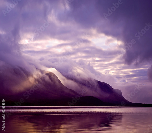 Landscape. Mountains and lake in mist in morning with purple col