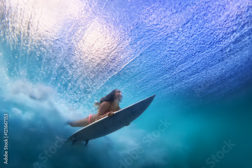 Sportive girl in bikini in action. Surfer with surf board dive underwater under breaking ocean wave. Healthy lifestyle. Water sport, swim and extreme surfing in adventure camp on summer beach vacation