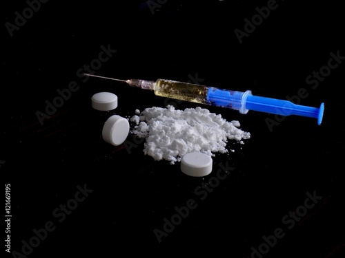 Cocaine drug powder pile, pills and injection on black background