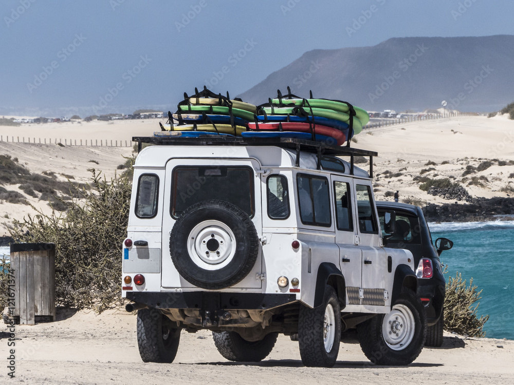 Surf school car with surf boards on top of the car.