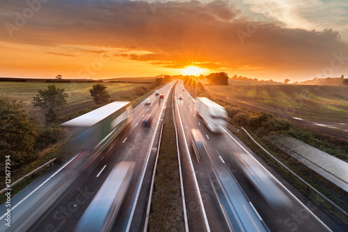 Trucks and Cars in Motion on Busy Motorway at Sunset photo