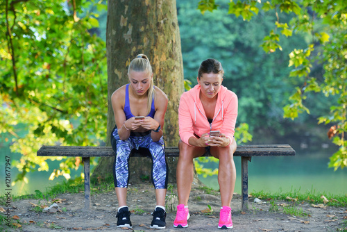 Shot of two females taking a quick break while out for a trail run using phone