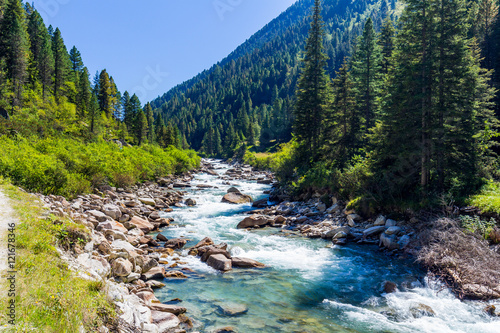 Austrian Alps. Starting famous Krimml waterfalls. Crystal clear water sparkles in the midday sun. Through the narrow creek wooden bridge spanned