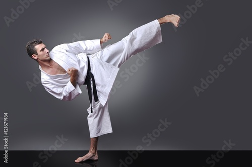 Handsome young black belt male karate doing kick on the gray background photo