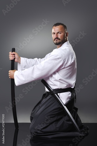 Handsome young black belt male karate posing with sword on the gray background