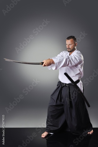 Handsome young black belt male karate posing with sword on the gray background