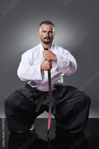 Handsome young black belt male karate posing with sword on the gray background