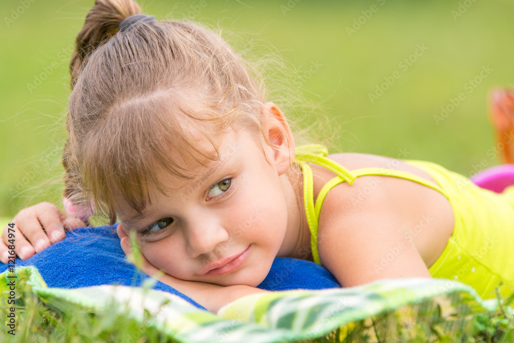 Five-year girl lies on a bed on a green meadow and thoughtfully looks aside Five-year girl lies on a bed on a green meadow and thoughtfully looks aside