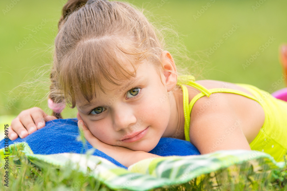Five-year girl lies on a bed on a green meadow and touching looking to the frame Five-year girl lies on a bed on a green meadow and touching looking to the frame