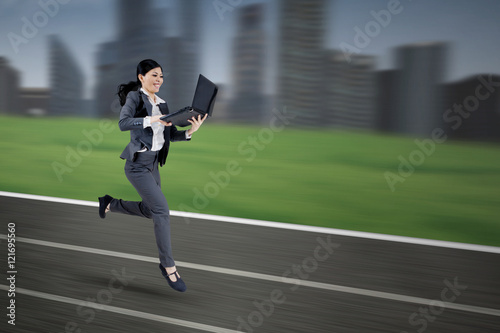 Businesswoman with laptop running on track © Creativa Images
