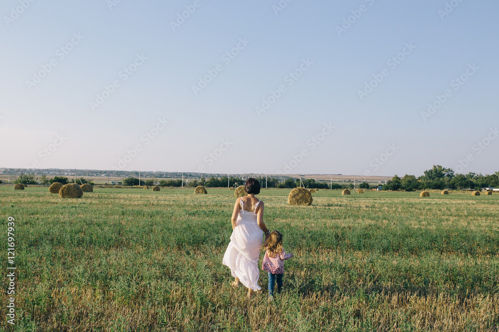 Pregnant woman in white dress walking with her daughter in the field