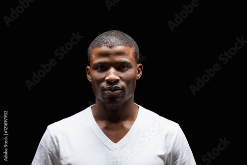 Portrait of handsome Afro-American man looking at camera in studio. Man in white T-shirt posing over black background.