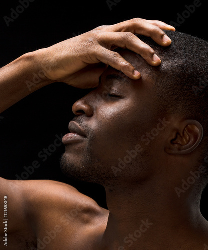 Closeup portrait of hanfsome naked passionate Afro-American man posing with his eyes closed over black background.