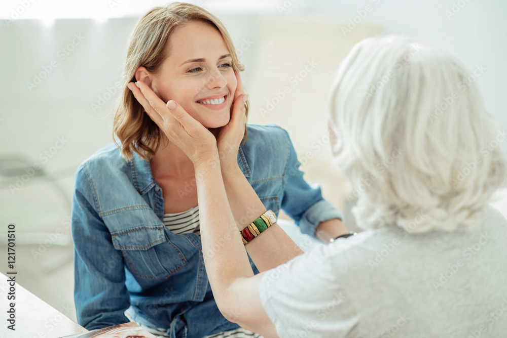 Pleasant aged woman holding cheeks of her adult daughter Pleasant aged woman holding cheeks of her adult daughter