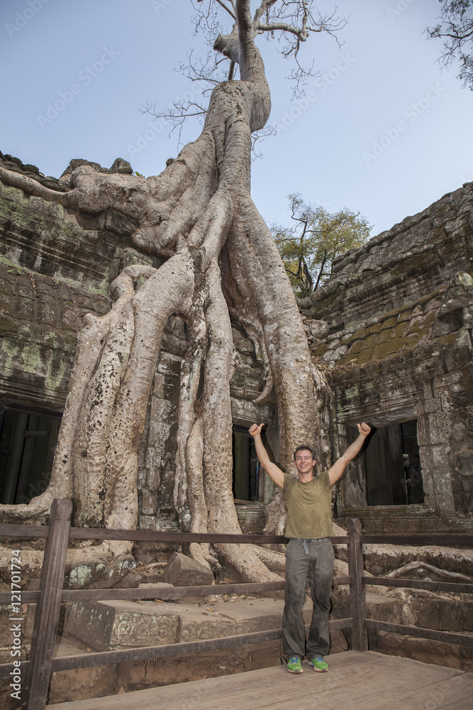Fototapeta premium Tourist at Ta Prohm temple in Angkor. Majestic spung tree grows throught the ancient walls of the temple