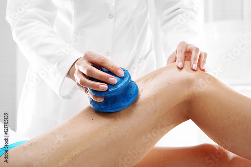 Drenaż limfatyczny.Kosmetyczka masuje uda kobiety gumowymi bańkami do masażu.