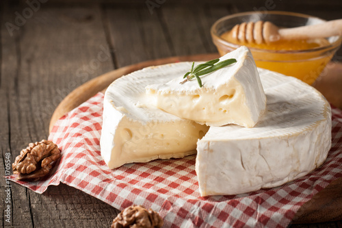 Brie type of cheese. Camembert cheese. Fresh Brie cheese and a slice on a wooden board with nuts, honey and leaves. Italian, French cheese. photo