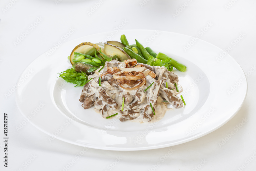 Liver Stroganoff on a plate with greens, beans and pickled cucumber      white background