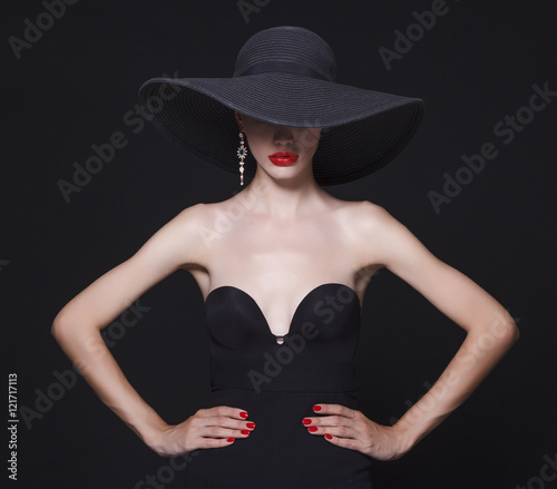 Luxury woman in a large black hat and bright lips on black background