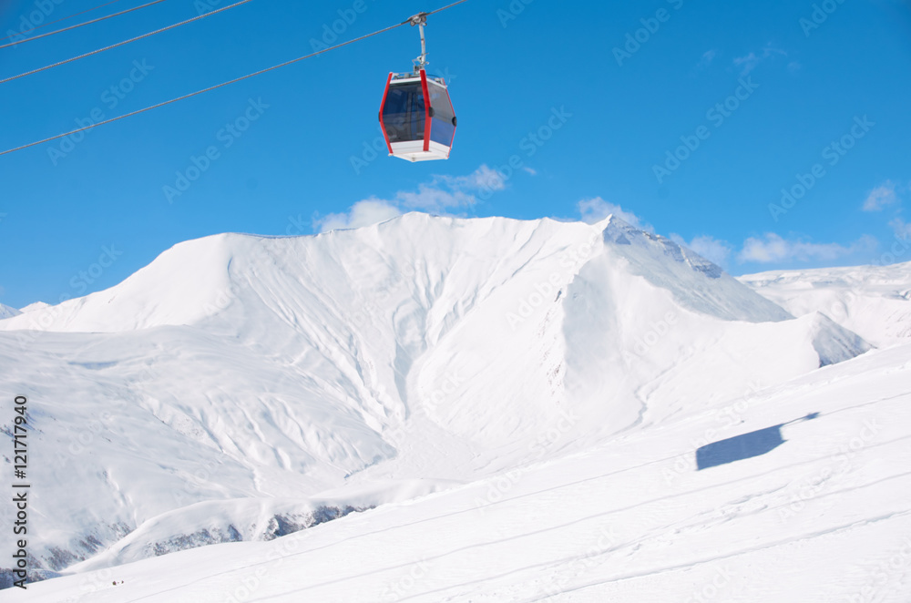 Cable lift for skiers or snowboarders in brigth day on ski resort with blue sky and white snowy mountains background. Copy space for a text. Red car. cabinet for athletes