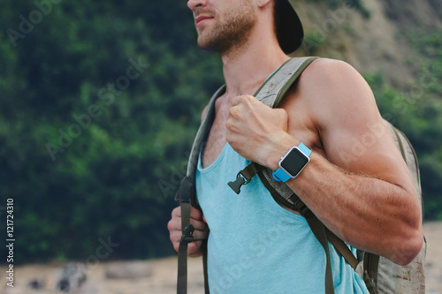 Young man with backpack walking on the beach and wearing smart watch