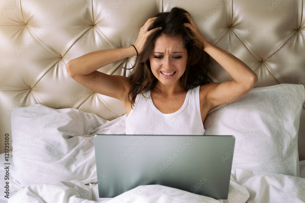 Young woman looking in laptop's screen and holding her head in confusion