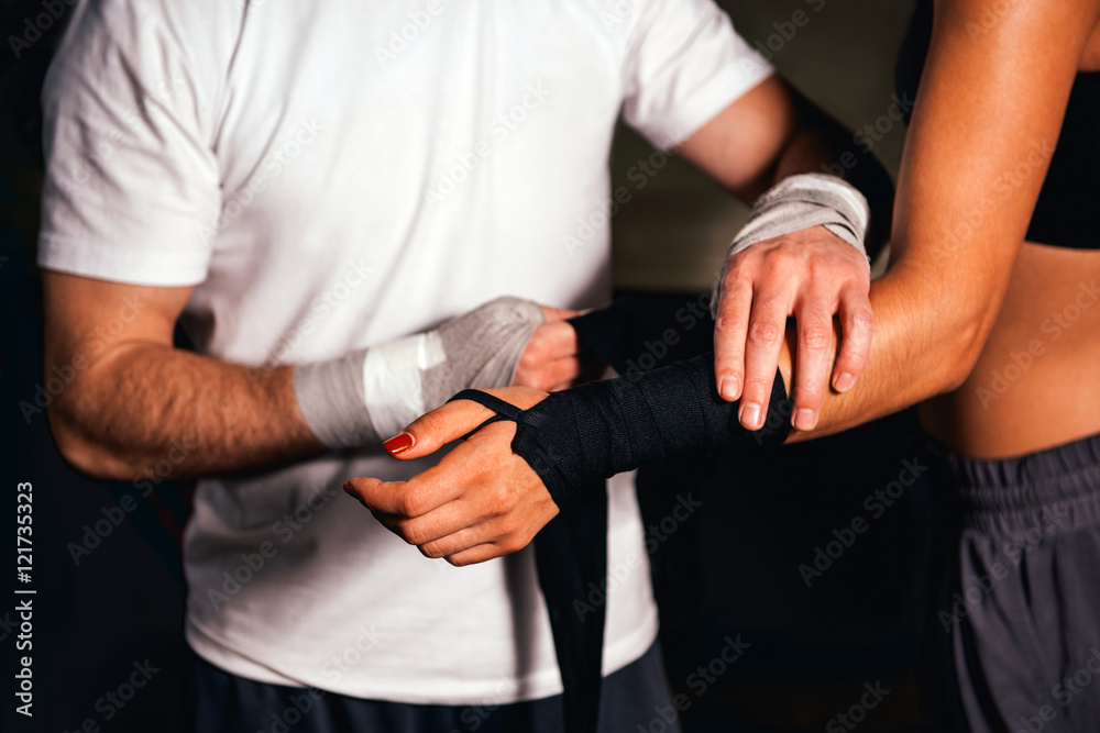 Personal trainer wrapping bandages around female boxers hand