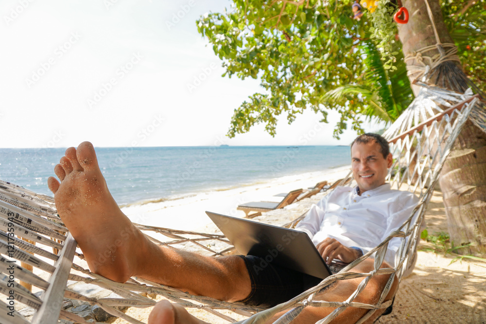 Young man work on laptop relaxing in hammock with seaview