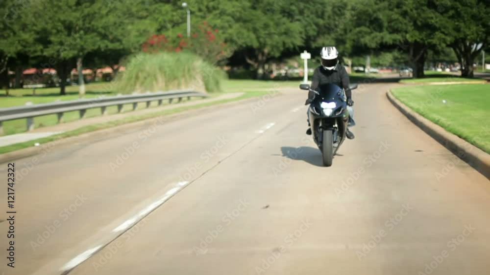 A motorcyclist turns out onto an avenue from a neighborhood street. A motorcyclist turns out onto an avenue from a neighborhood street.