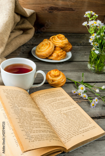 Cozy breakfast in spring or early autumn tea, freshly baked scones and bouquet of field's daisy and fascinating book. Copy space photo