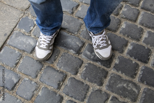 Teenage legs in sneakers and blue jeans standing on paving stones, top view, unusual perspective