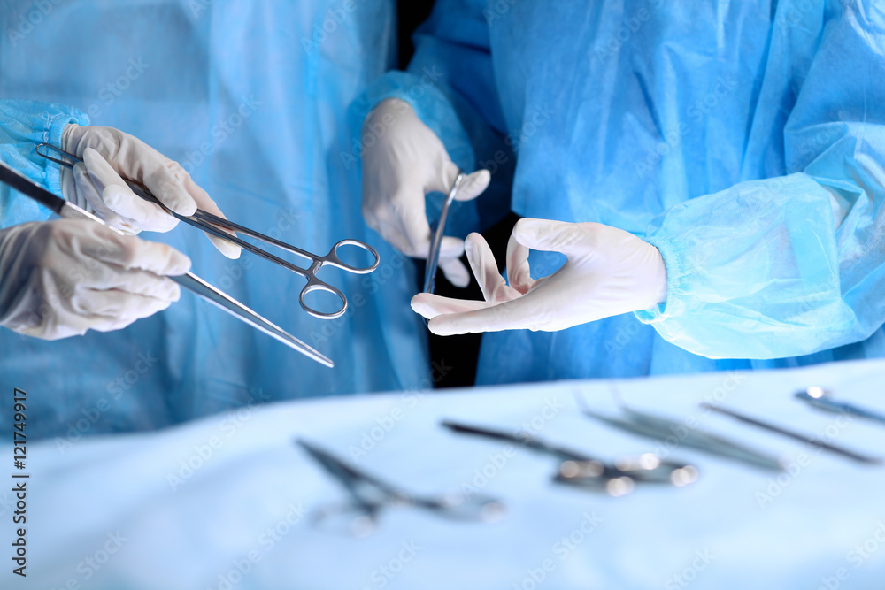 Medical team performing operation. Group of surgeon is working in operating theatre toned in blue Medical team performing operation. Group of surgeon is working in operating theatre toned in blue