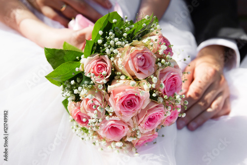 Bride and groom hands with pink roses bouquet. Closeup