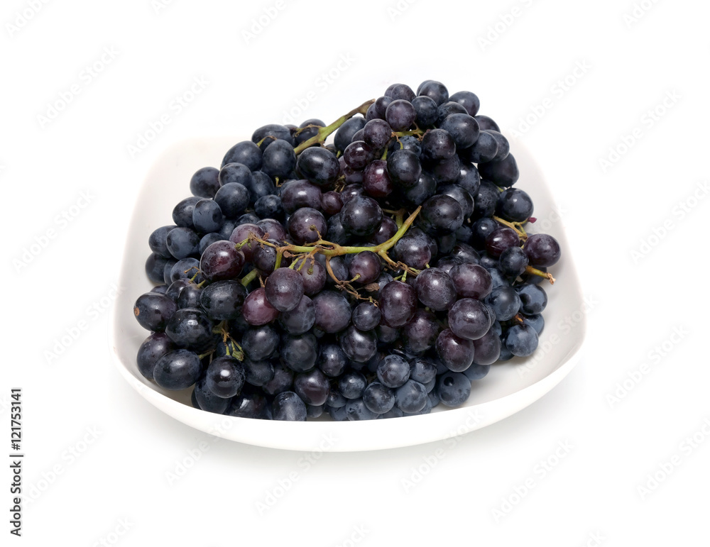 Lot of ripe wine grape bunches with black berries in square bowl isolated on white background close up Lot of ripe wine grape bunches with black berries in square bowl isolated on white background close up