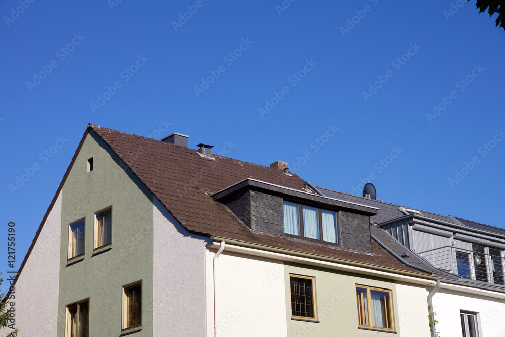 House with dormer windows and tree on the top right corner against a blue sky
