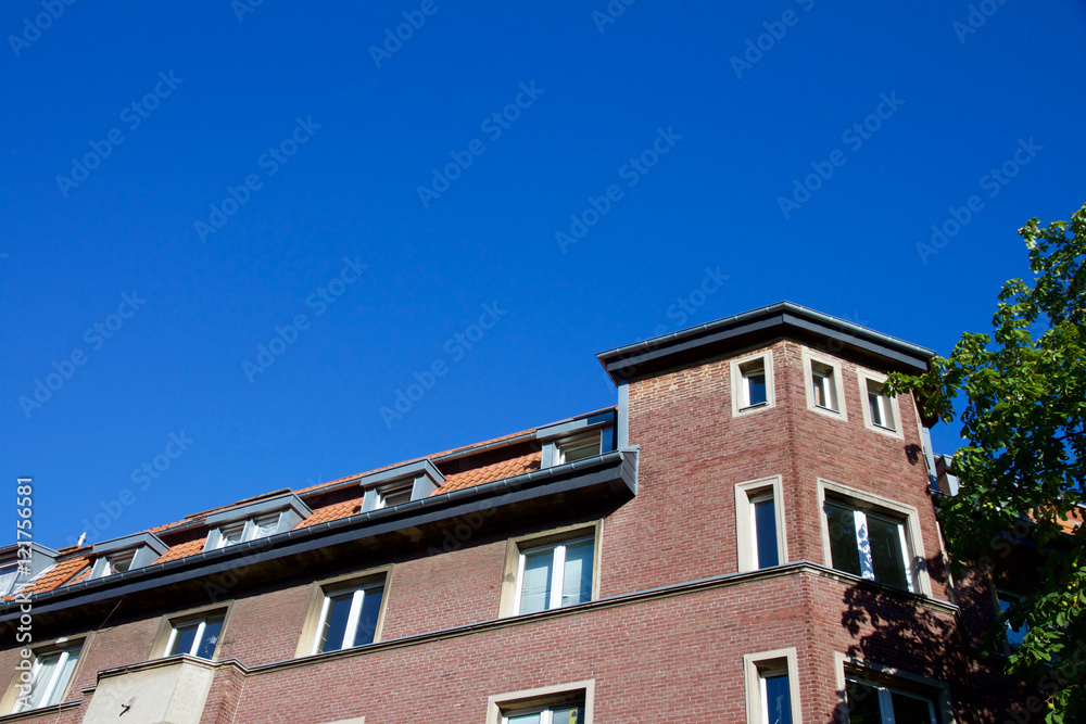 Facade of a red house and tree against a blue sky in Aachen, Germany