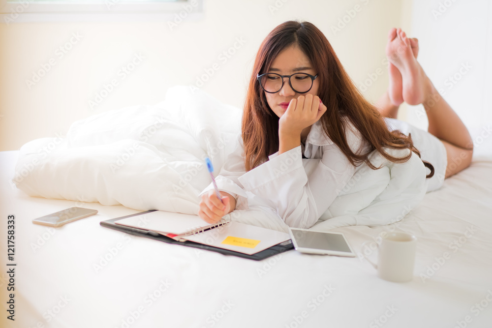 Smiling woman writing notes lying in bed Smiling woman writing notes lying in bed