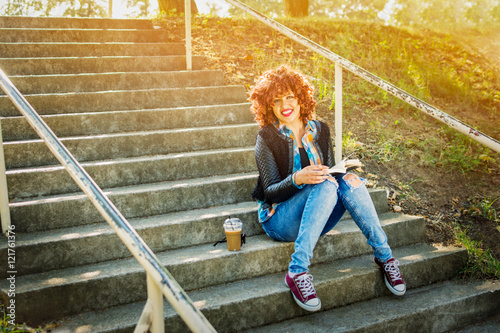 Cool teenage girl reading a book outdoors sitting on stairs