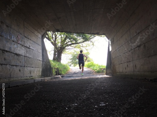 Runner exiting dark tunnel into summer light