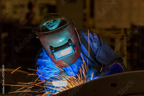 Welder with protective mask welding metal and sparks in car factory