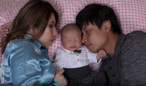 Young couple sleeping with infant baby in bed