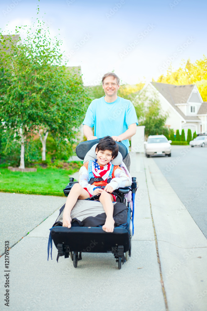 Father pushing ten year old disabled son in wheelchair outdoors Father pushing ten year old disabled son in wheelchair outdoors