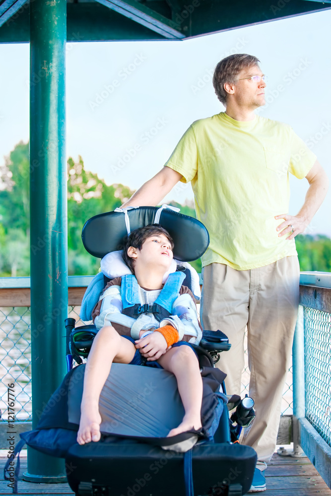 Father sitting by lake with disabled son in wheelchair
