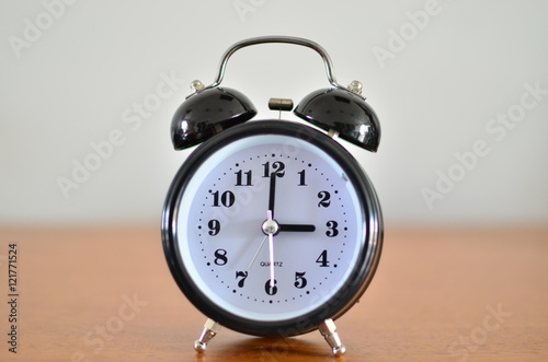 The black alarm clock is showing time at three o'clock