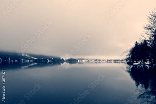 Winter landscape on the lake in black and white, with trees reflecting on still water surface. Monochrome image filtered in nostalgic, vintage style with soft focus and red filter; high contrast.