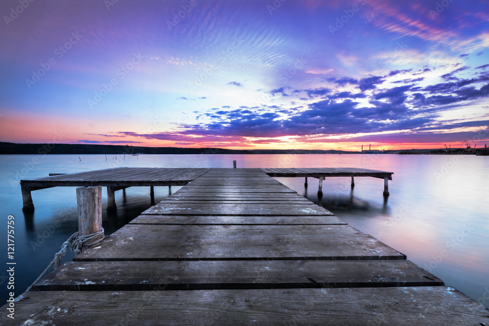 Wooden pier on a blue lake sunset and smooth reflection on water