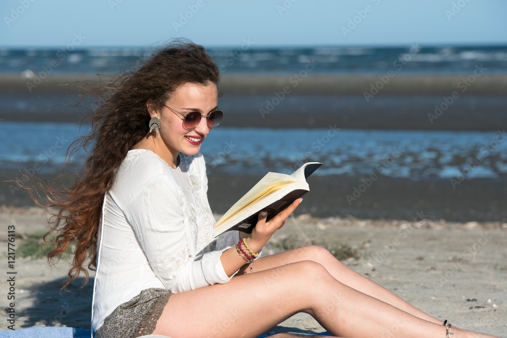 Woman with long curly hair reading a book at the beach