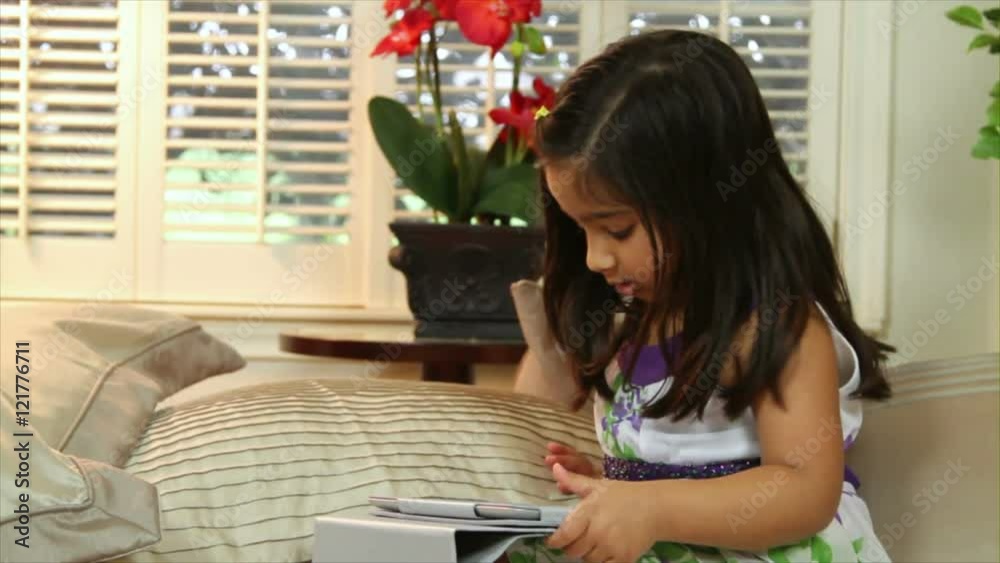 A cute little Indian child intrigued by what she sees on her electronic tablet looks up and smiles. A cute little Indian child intrigued by what she sees on her electronic tablet looks up and smiles.